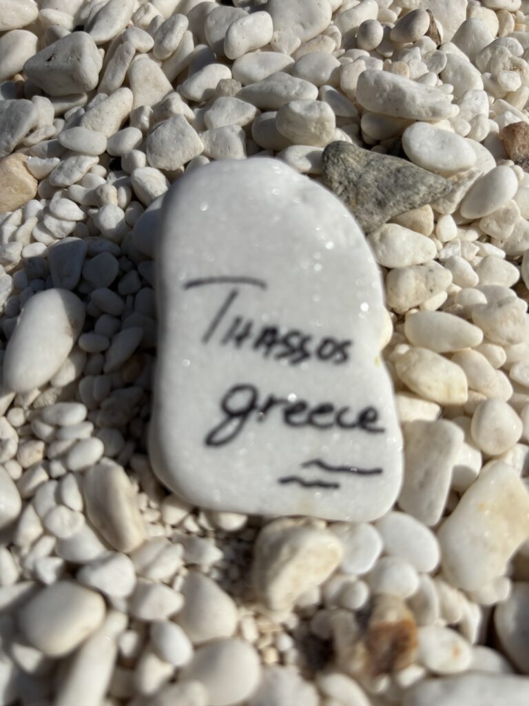White marble stone with Thassos Greece written on it on a beach in Thassos.